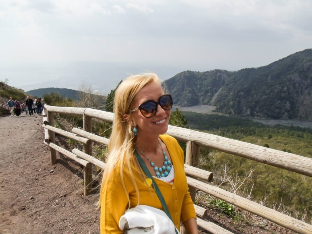 An image of Lindsey with blonde hair, walking up Mount Vesuvius. She's wearing a yellow cardigan over a white tank top.