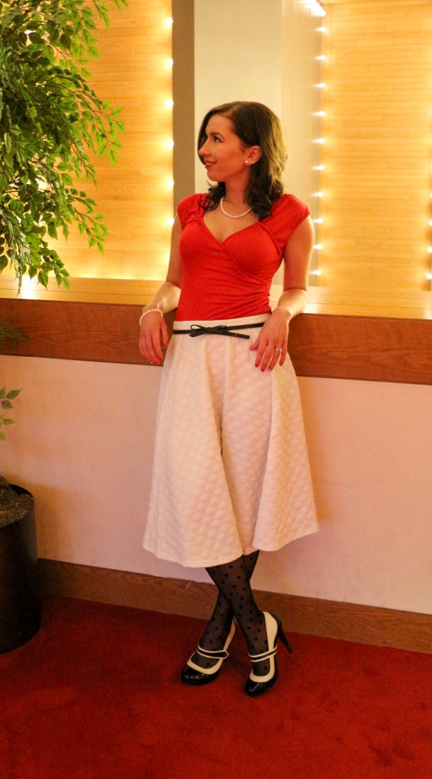 Lindsey wearing a red shirt, white midi skirt and black heels