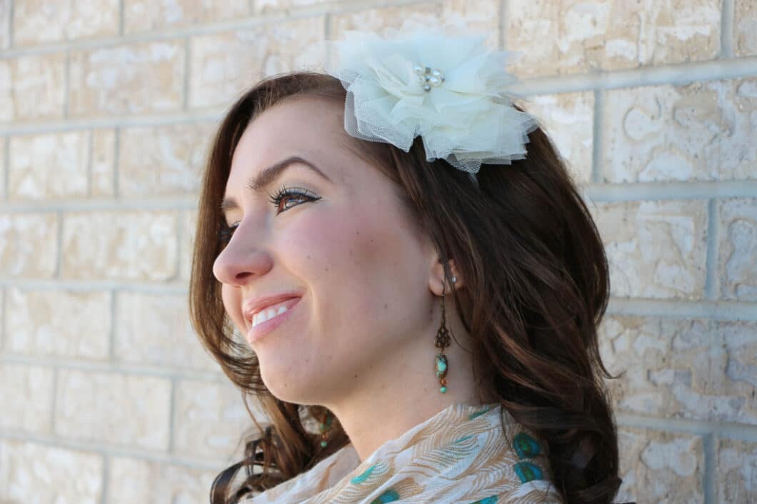 A side-profile image of Lindsey from Have Clothes, Will Travel. She's wearing a fabric flower barrette in her hair and has long, wispy eyelashes.