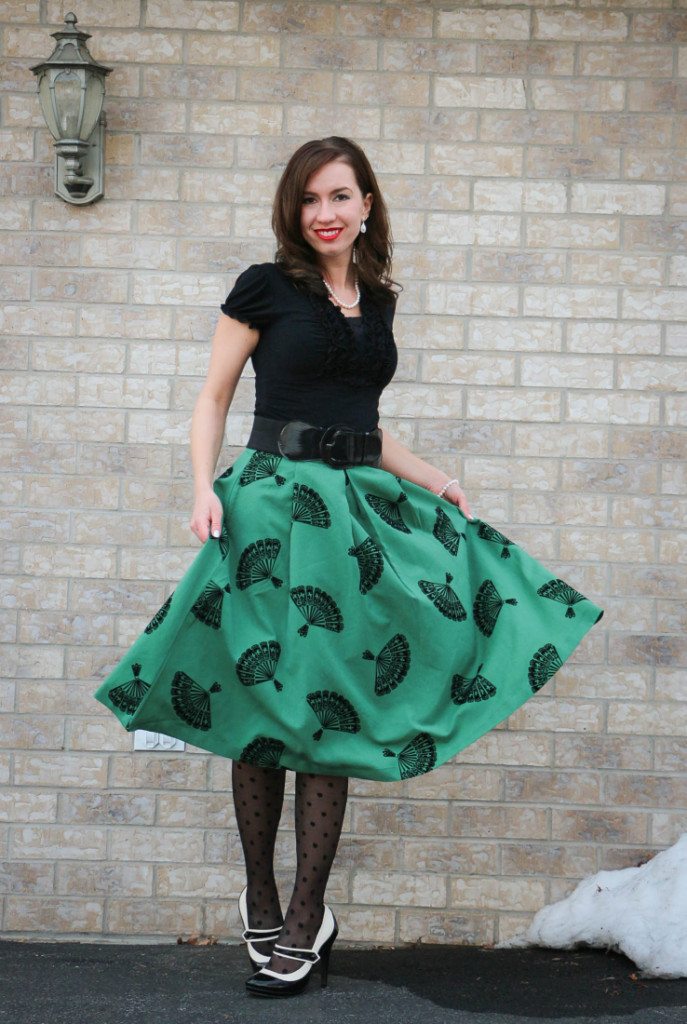 Lindsey wearing a black shirt with green midi fan skirt, black polka dot tights and black and white heels