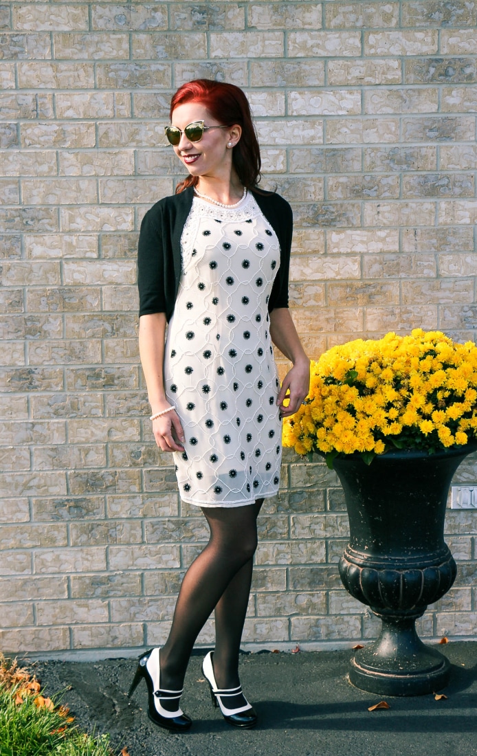 Lindsey with red hair wearing a cream polka dot dress with black tights and black and white high heels
