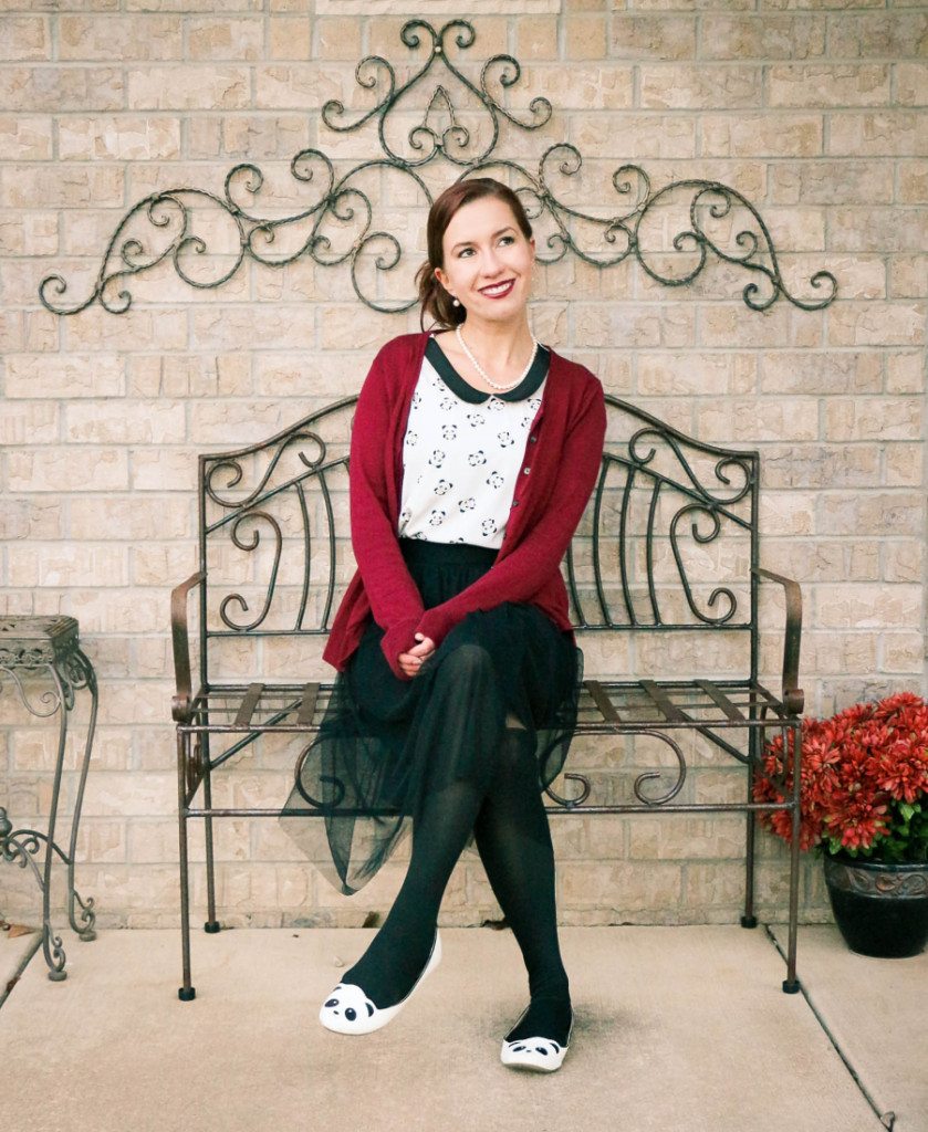 Lindsey sitting on a bench wearing a panda shirt with peter pan collar, tulle black skirt, panda flats, and black tights