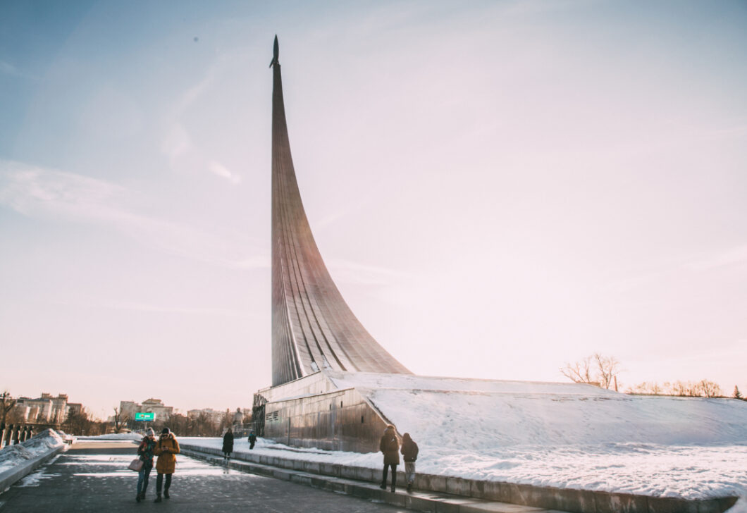 A giant art installation called Monument to the Conquerors of Space in Moscow, Russia. The monument is a giant metal curve that shoots up into the air. Visitors admire the monument on a snowy day.
