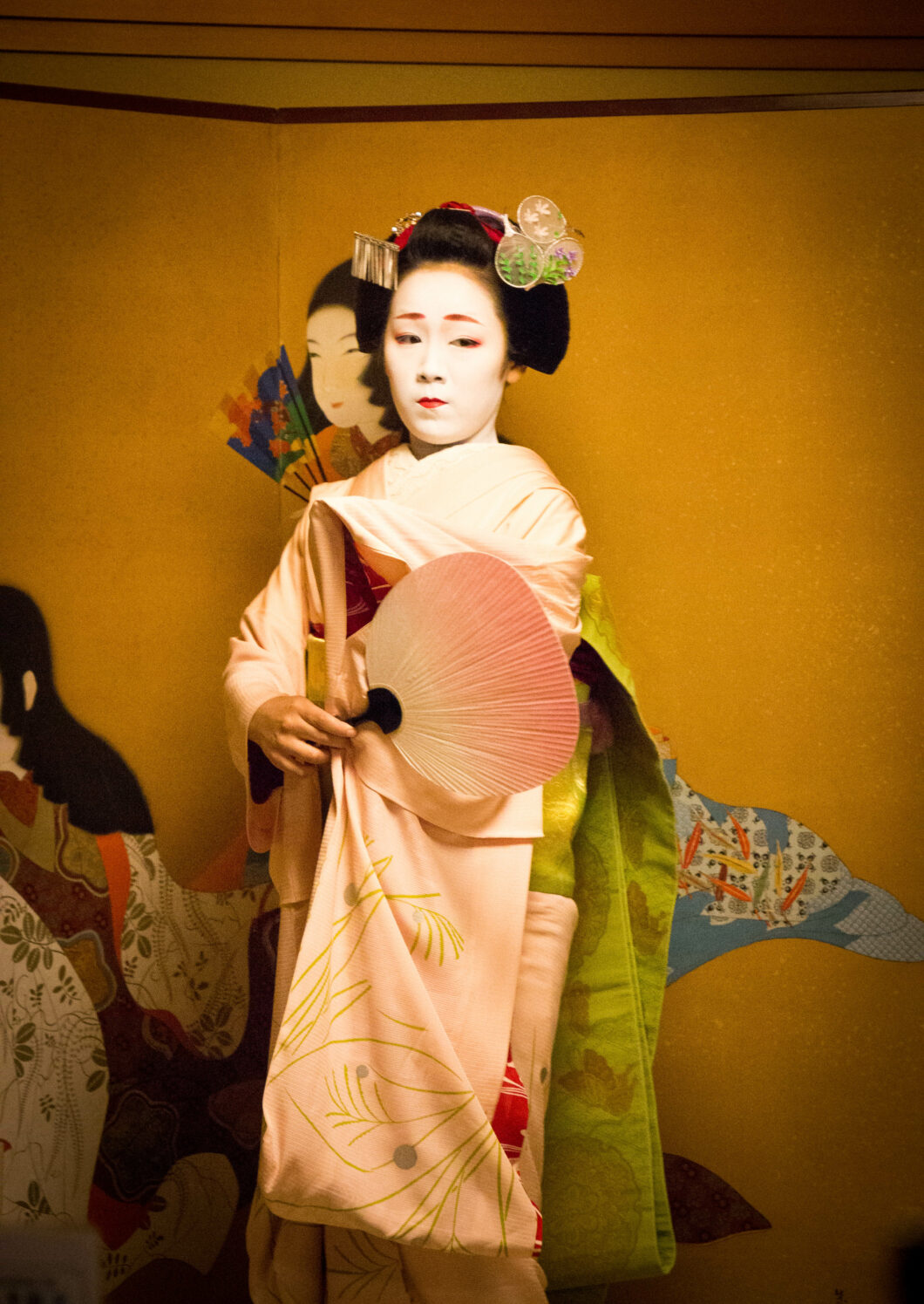 A young girl dressed in traditional Maiko clothing dances with a fan during a performance.