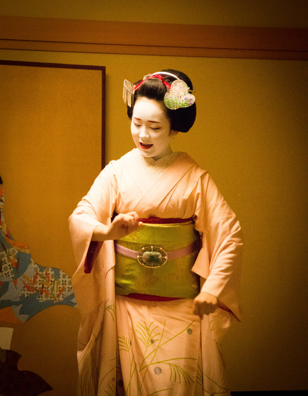 A Japanese Maiko dances to music during an evening dinner performance. She is wearing traditional Geisha clothing including a kimono and obi sash.
