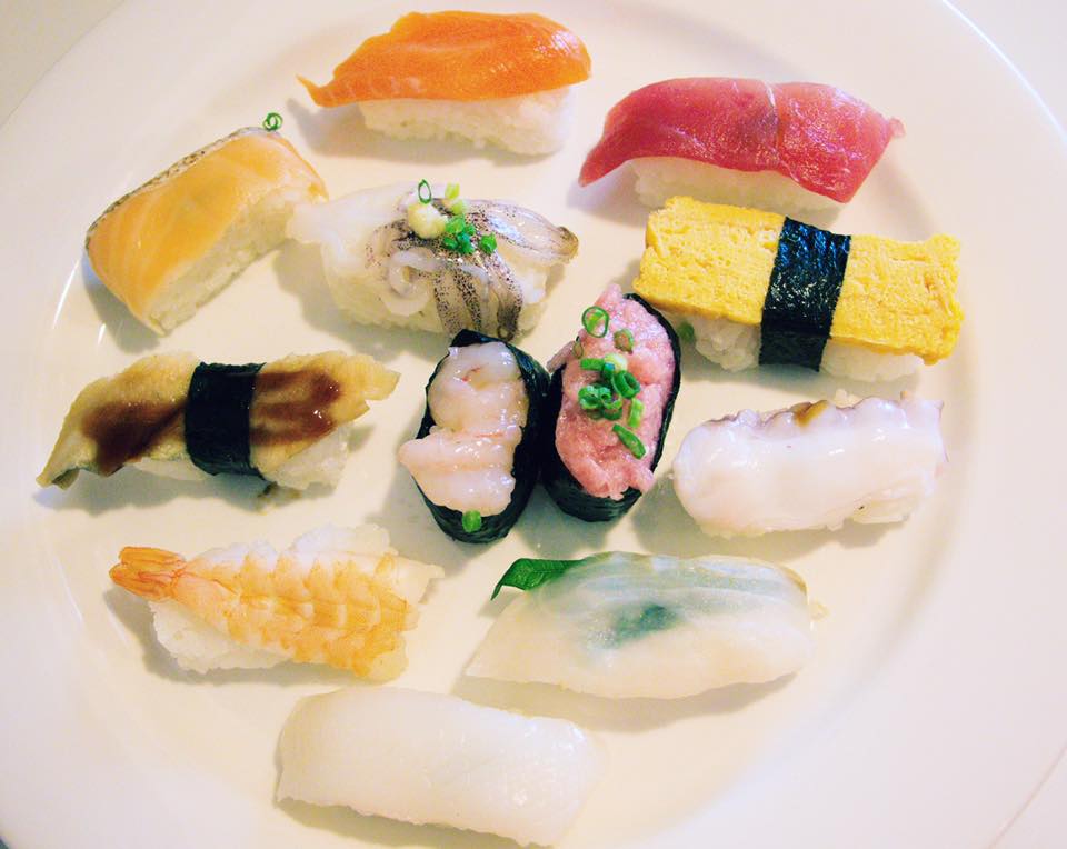 A variety of sashimi and nigiri sushi arranged on a white plate. The sushi is made with pieces of raw fish on top of a ball of sushi rice.