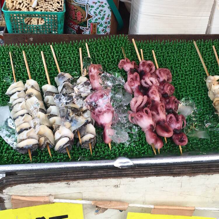 Skewers of food rest on a green mat at a street food stand in Tokyo.