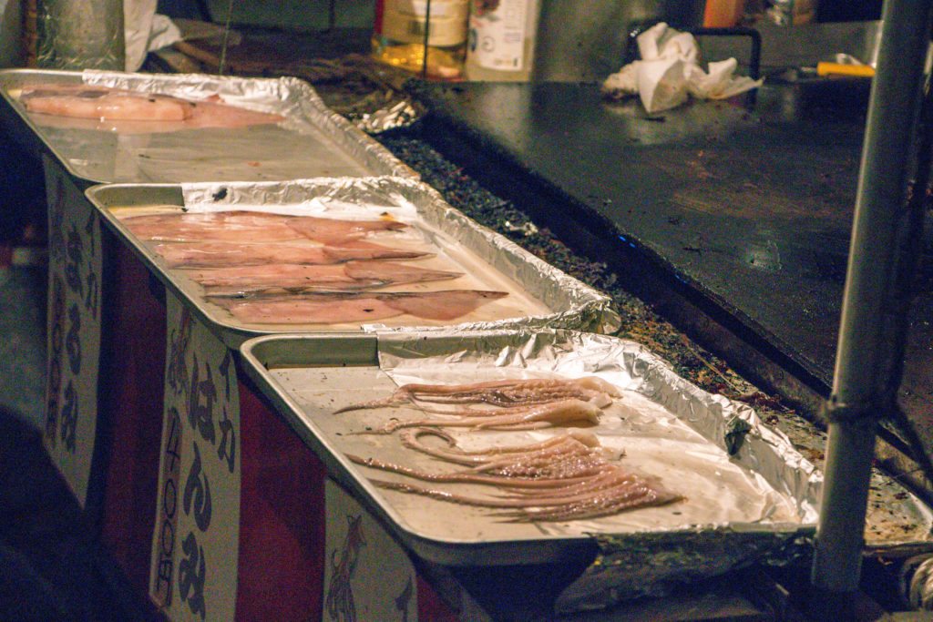 Trays of meat and seafood prepared for cooking at a Tokyo street food stand.