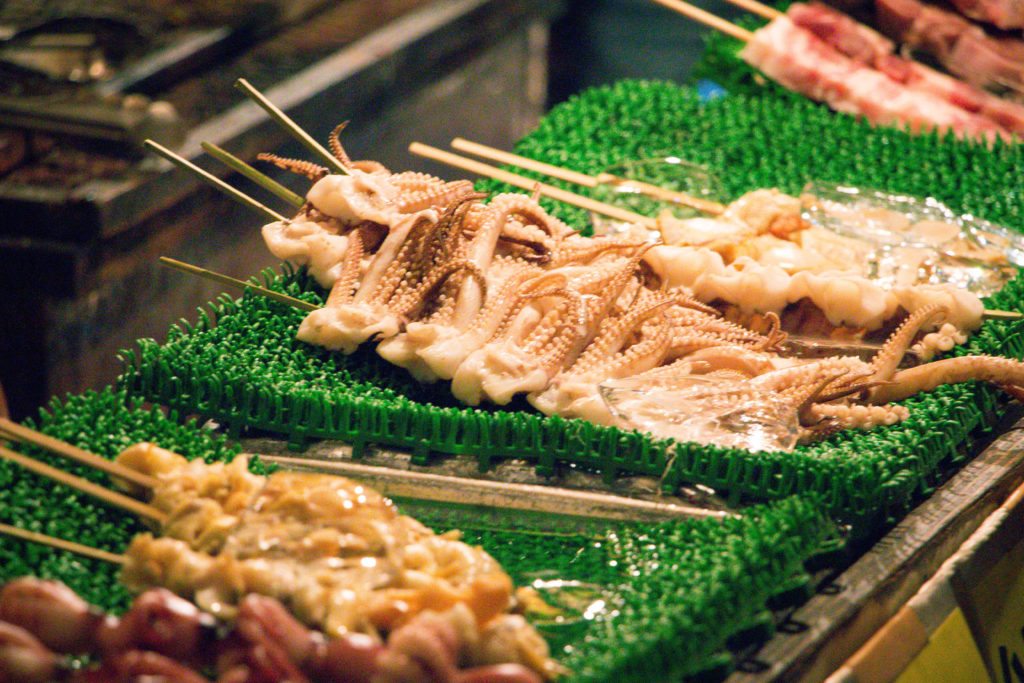 Skewers of tiny squid lined up, ready to cook at a street food stand in Japan.