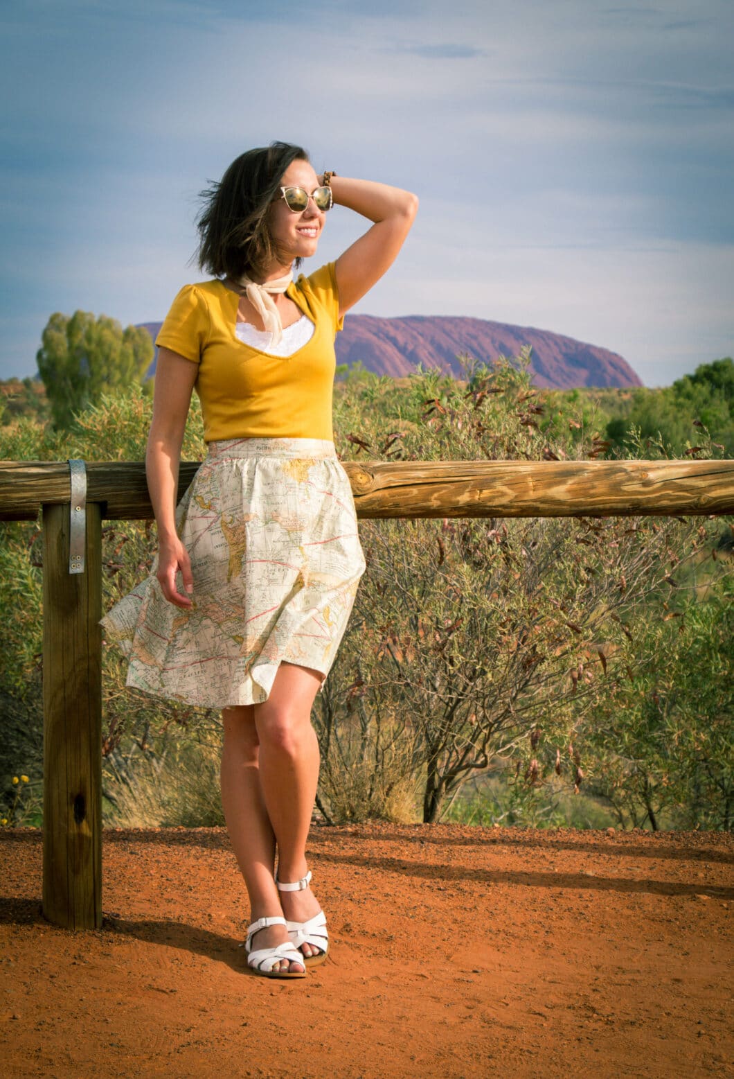 Women wearing map skirt modcloth, yellow top with a scarf and sunglasses and white sandals 