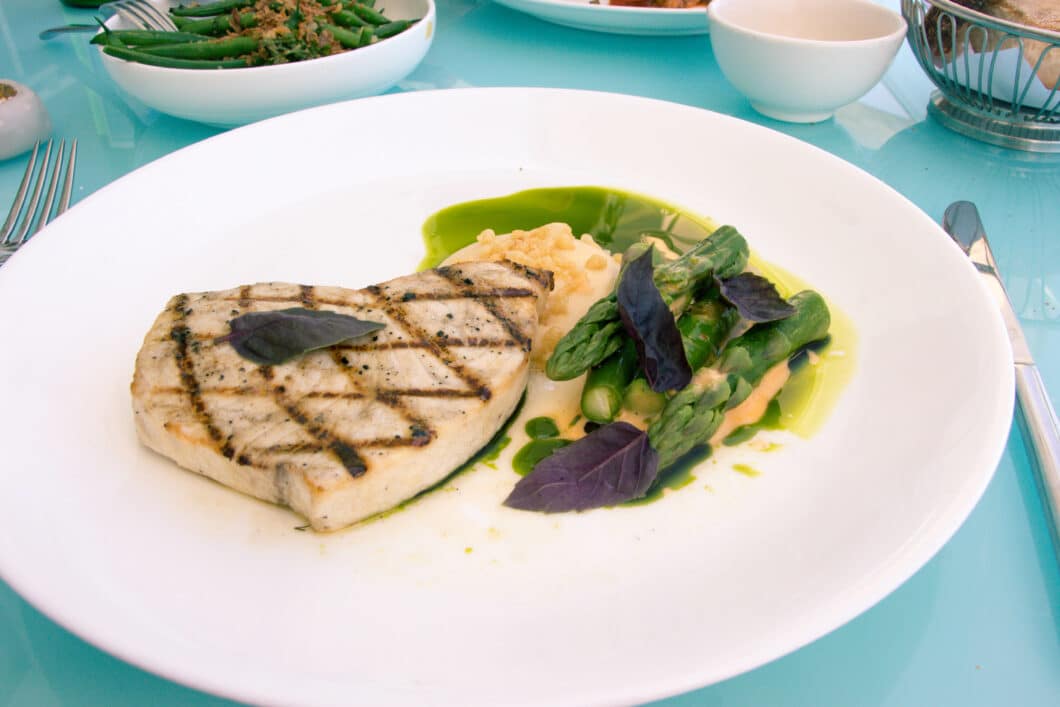 A fillet of white fish served with a small side salad and dressing, served on a white plate.