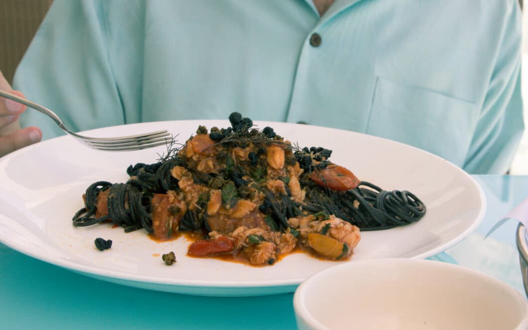 A plate of spaghetti al nero e granchip - black spaghetti noodles tossed with vegetables and sauce, served on a white plate.