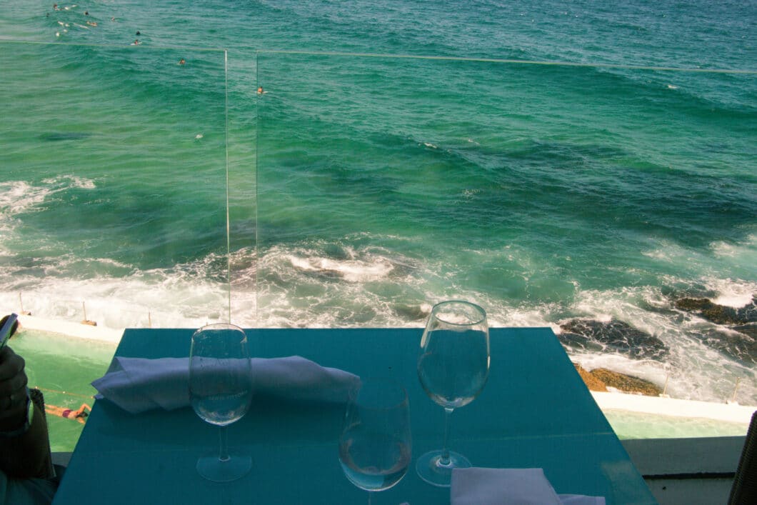 A table for two at Bondi Icebergs restaurant overlooks the ocean, where you can see people swimming in the waves.