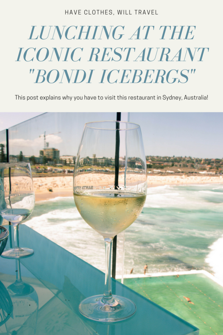 A wine class sits on the corner of a table, overlooking Bondi beach. Text across the image reads, :Lunching at the iconic restaurant Bondi Icebergs"