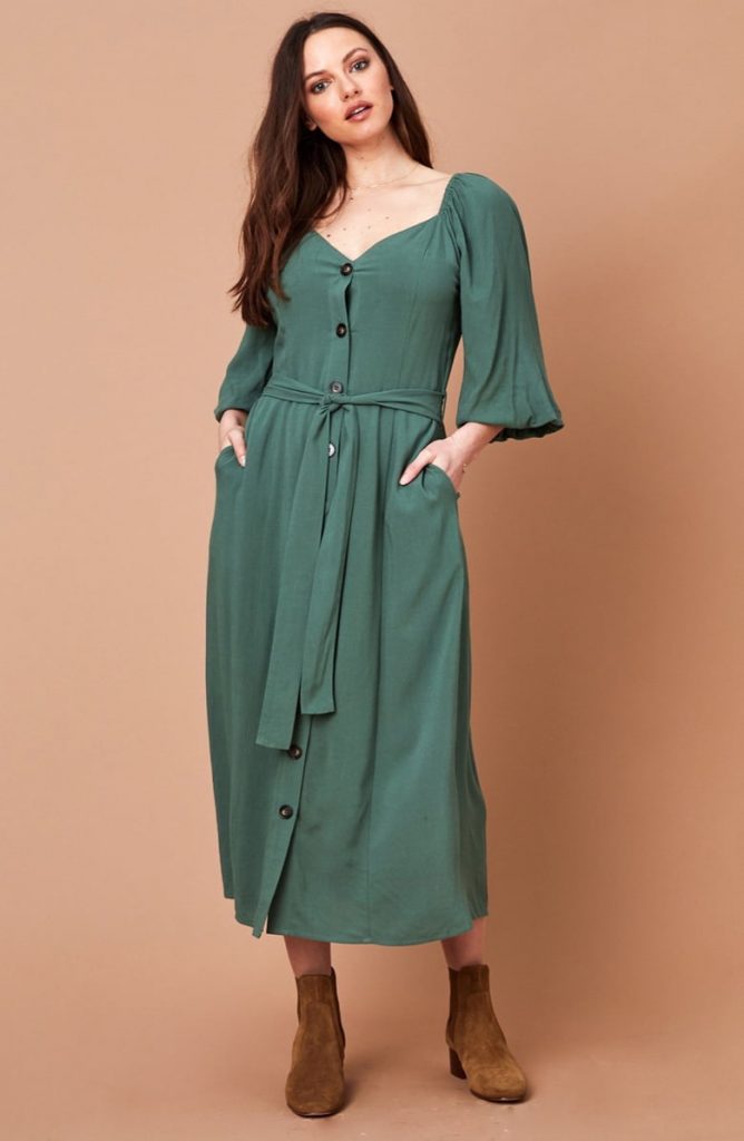 A woman with long dark hair wears a green midi dress with long sleeves