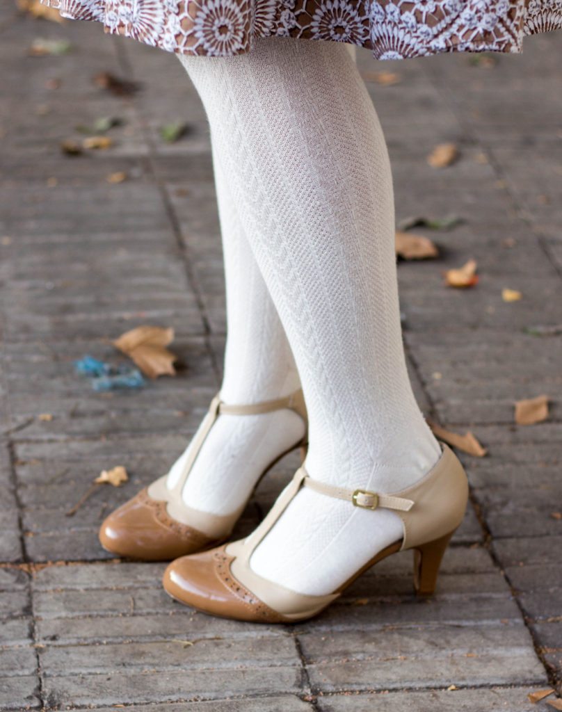 A close up image shows a woman's nude vintage style t-strap heels over white knit tights.