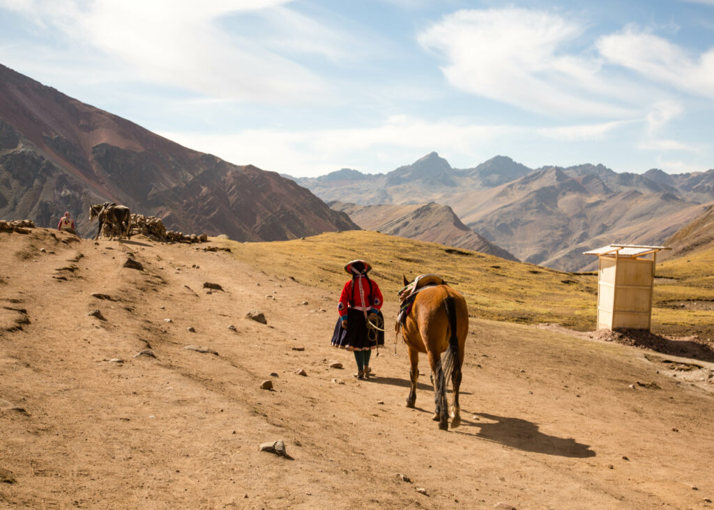 A woman walking a horse on a dirt path at rainbow mountains.