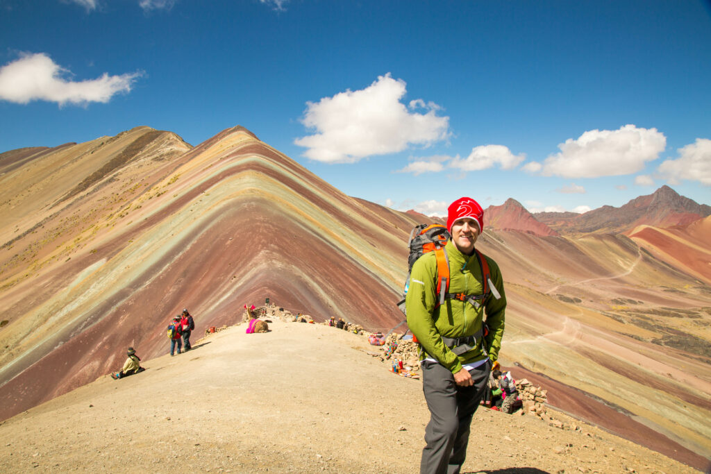 A man standing in front of a rainbow mountain.