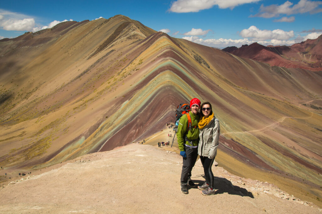 A Couple smiling at the camera with Rainbow mountain, Peru in the background