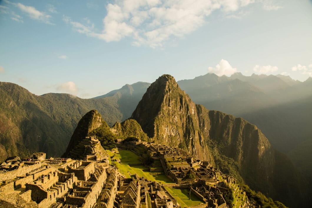 A professional photo of the village of Machu Picchu, surrounded by mountains on a clear, sunny day.