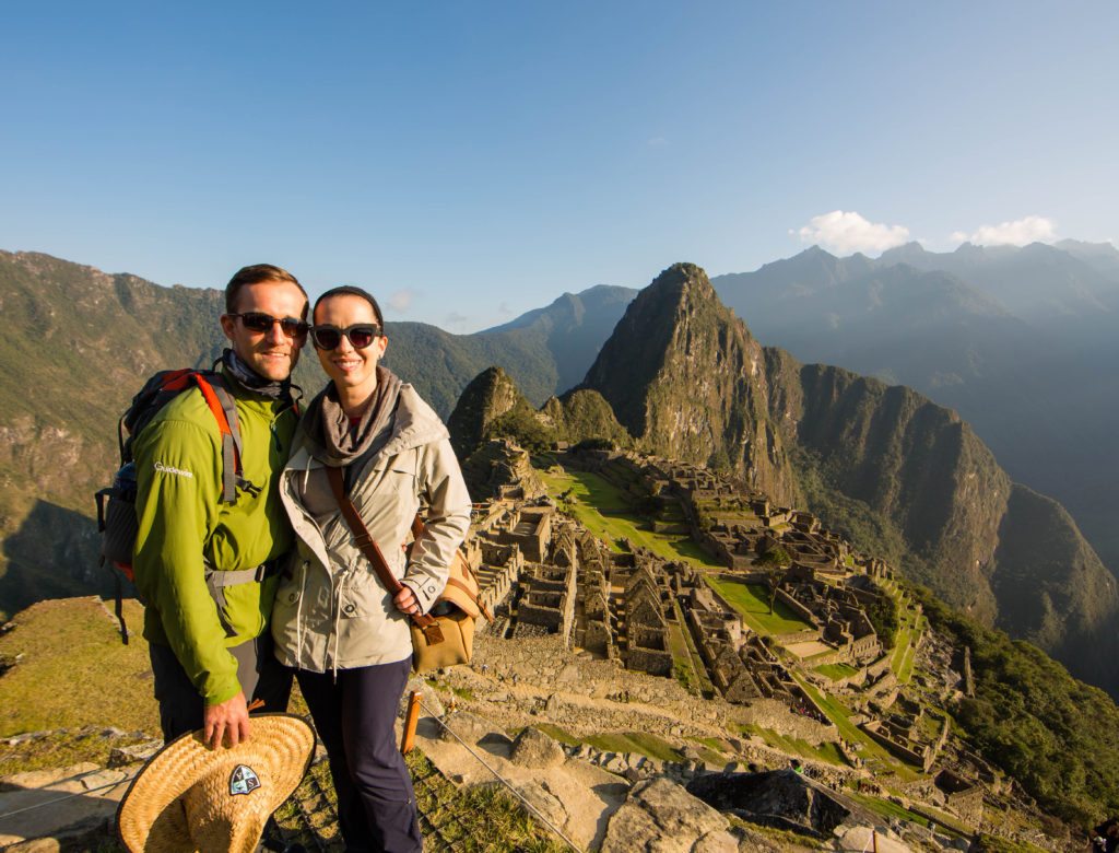 A couple smiling towards the camera with Machu Picchu in the background.