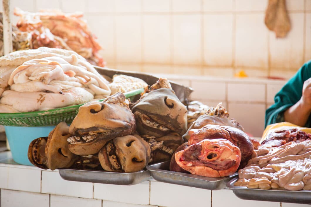 A woman is standing in front of a counter full of meat at San Pedro Market.