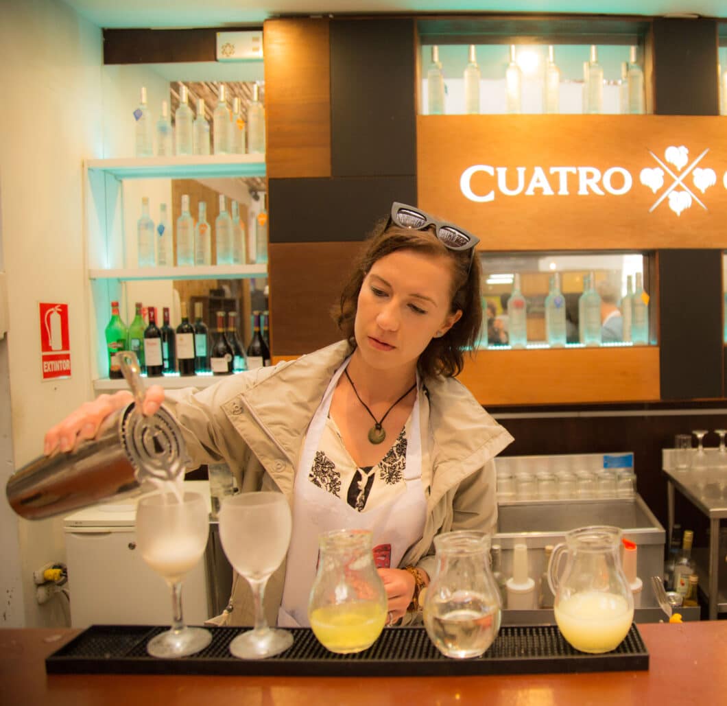 A woman pouring drinks and learning how to make a pisco sour.