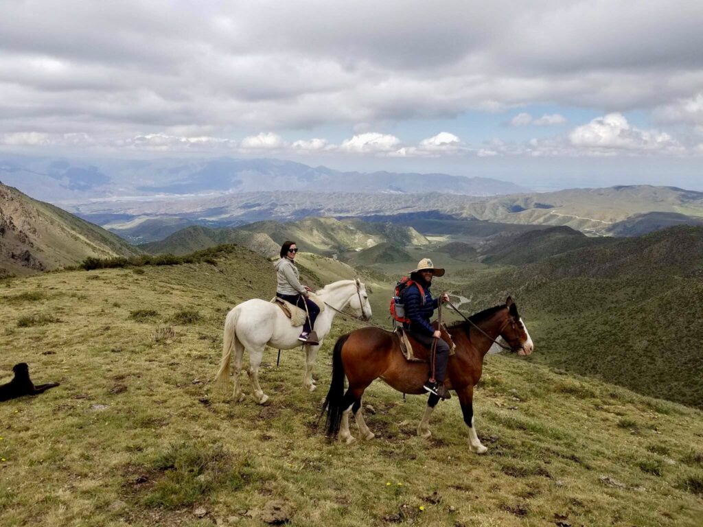 A man with a hat and a woman with sunglasses riding horses through the Andes in Argement.
