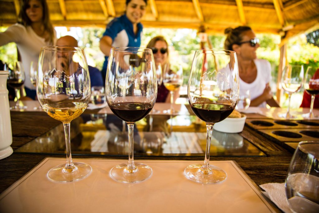 Three glasses of wine with people smiling in the background and being served at Kaiken winery, Argentina.