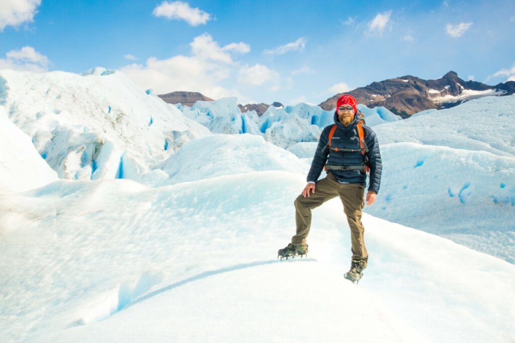 Zac standing on Perito Moreno Glacier wearing a blue coat and hiking pants