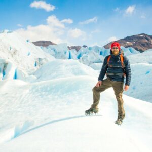 Zac standing on Perito Moreno Glacier wearing a blue coat and hiking pants