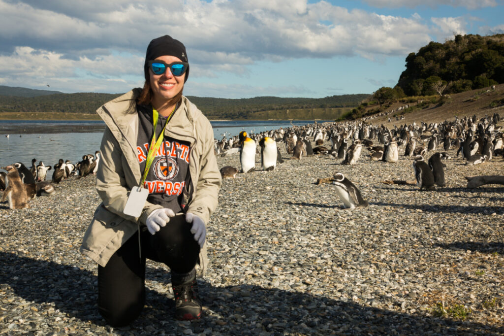 A woman kneeling in front of a group of penguins on Martillo Island, Argentina.