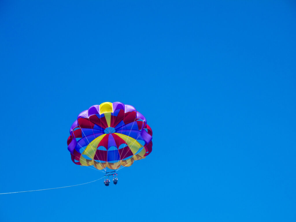 Two riders are in a red, blue, and yellow parasail soaring against a clear blue sky. 