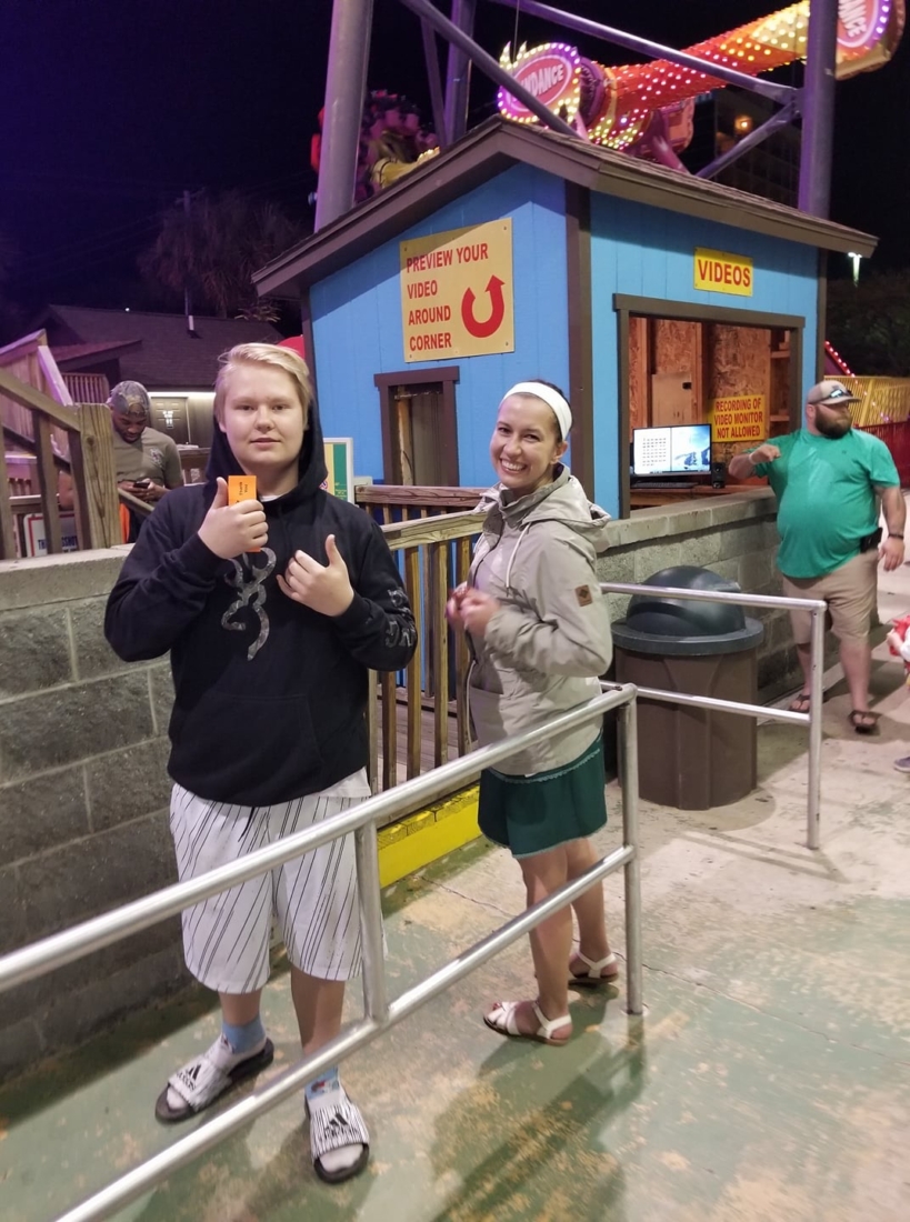 A teenage boy and adult woman giving the thumbs up as they wait in line in Myrtle Beach for amusement park rides 