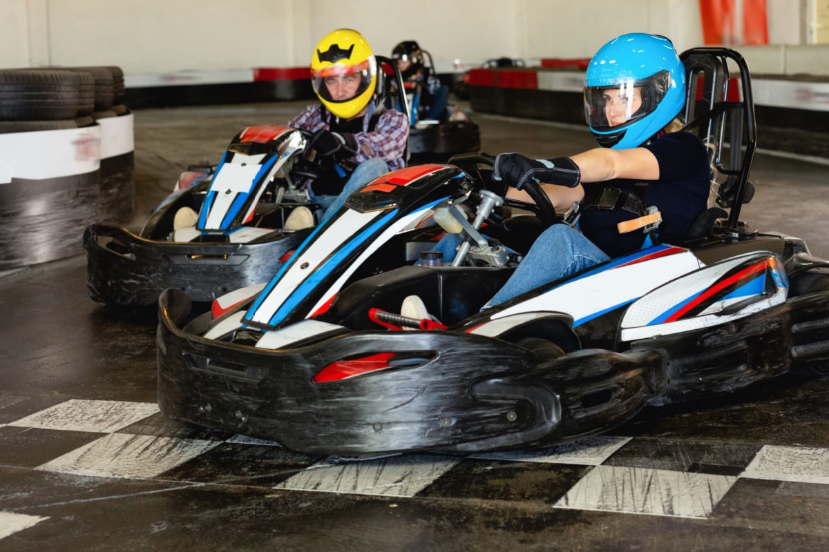 Group of positive smiling people driving go-carts at racing track