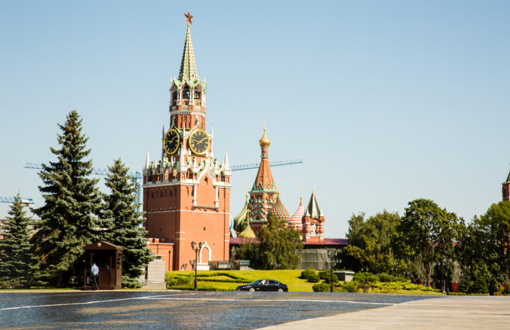 An exterior shot of the Kremlin Armoury - a large red brick building with a tall, ornate steeple. The building is surrounded by a lush lawn and tall trees.
