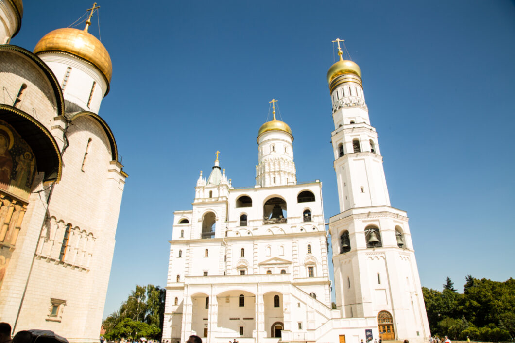 An exterior image of the Ivan the Great Bell Tower. The exterior of the building fs made of white stone and gold trim and houses 22 bells.