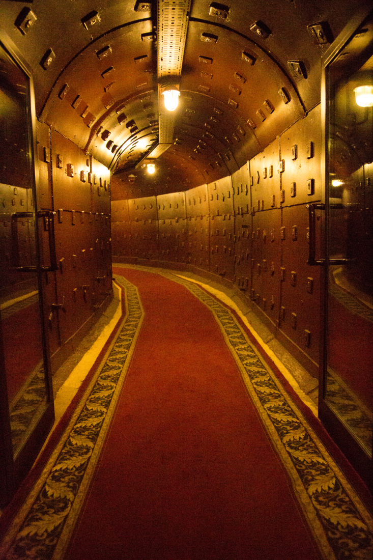 A long, curing hallway that's actually a metal-lined bunker from the Cold War era. The long hallway is carpeted and lit with overhead lighting.