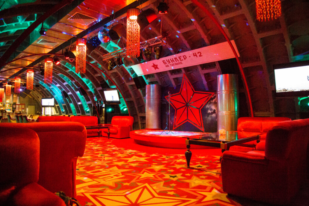 The Bunker 42 restaurant, an underground restaurant in Moscow. There are lounge chairs and Russian stars on the carpet and throughout the decor. The lighting is a rich red hue.