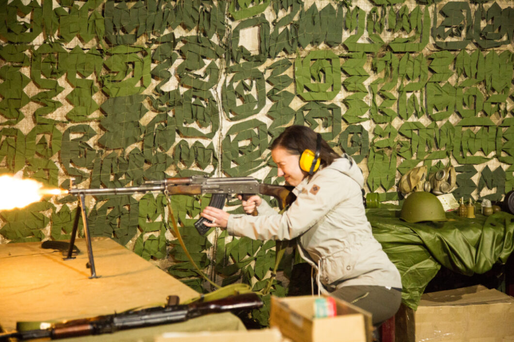 A woman shoots a mounted AK-47 machine gun at a shooting range.