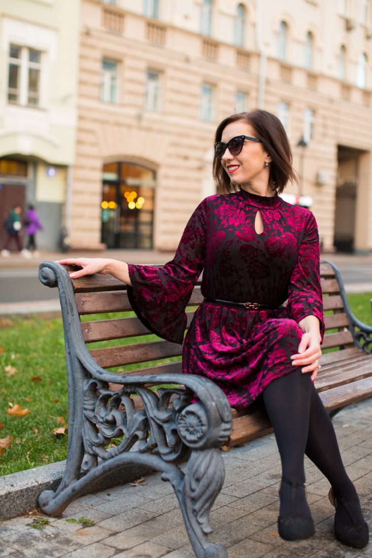 A velvet dress paired with black tights and suede pumps by a woman sitting on a park bench in Moscow