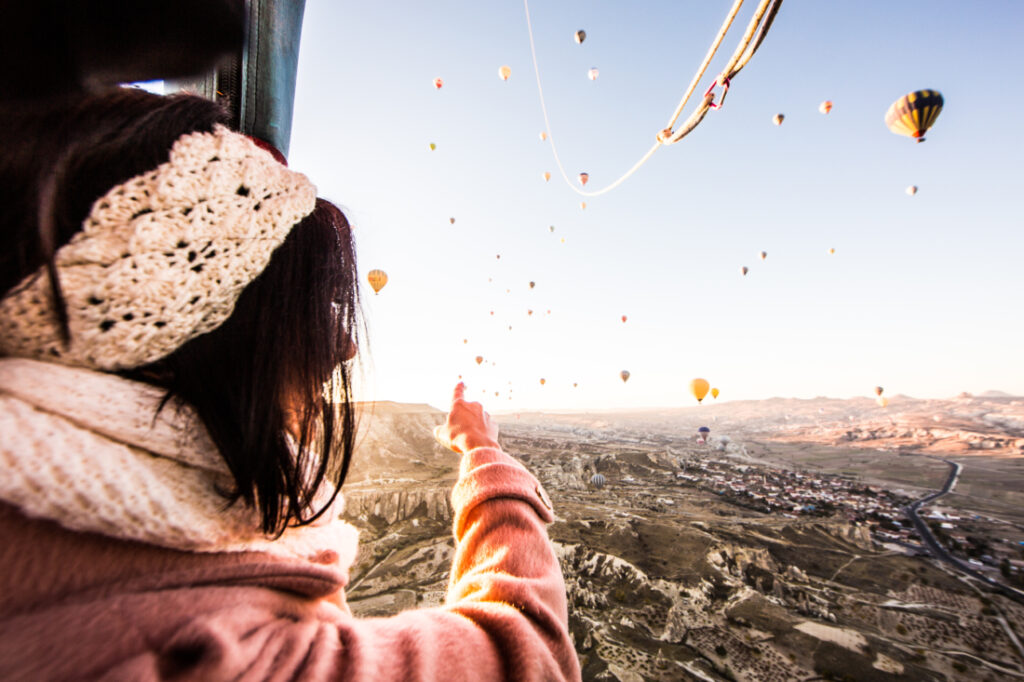 A woman on a hot air balloon looking at other hot air balloons in Cappadocia and pointing.