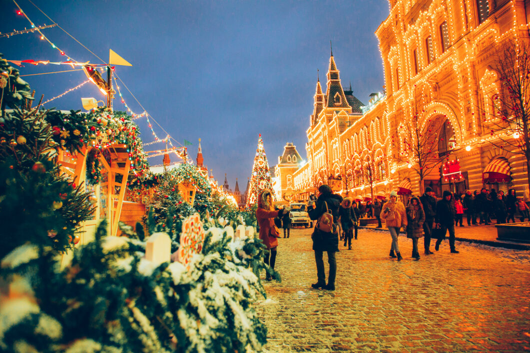 A Christmas market is filled with tourists walking down the street in front of the Russian Embassy Building in Moscow, Russia at Christmastime.