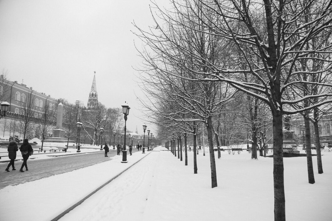 A snow-covered street in Moscow Russia at Christmas. Patrons walk down the empty road next to a park filled with snow-covered trees.