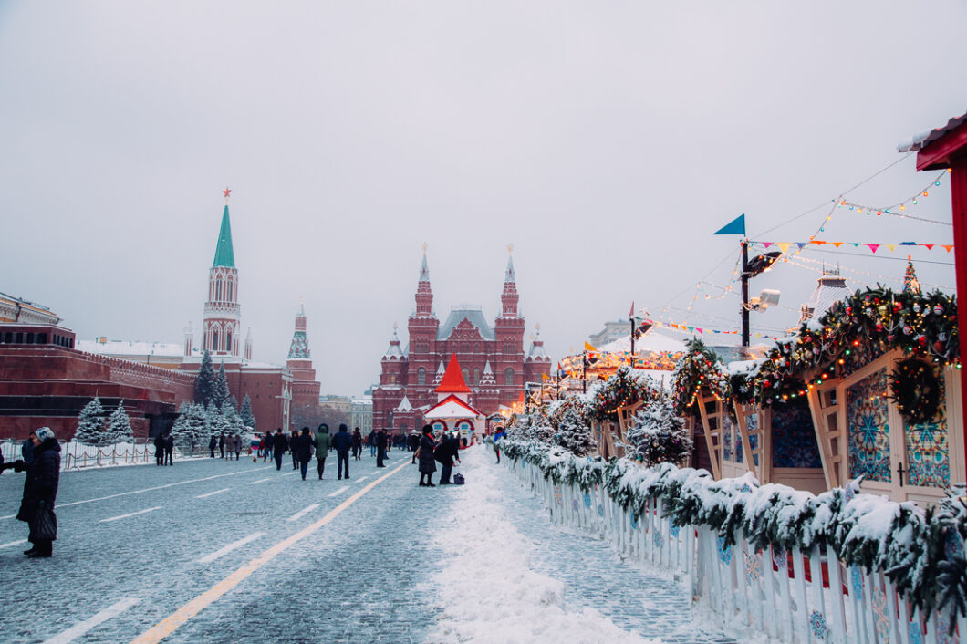 Moscow's Red Square at Christmas, with the Moscow Christmas market on the right side of the street and the Red Square buildings down a snow-covered street in the background.