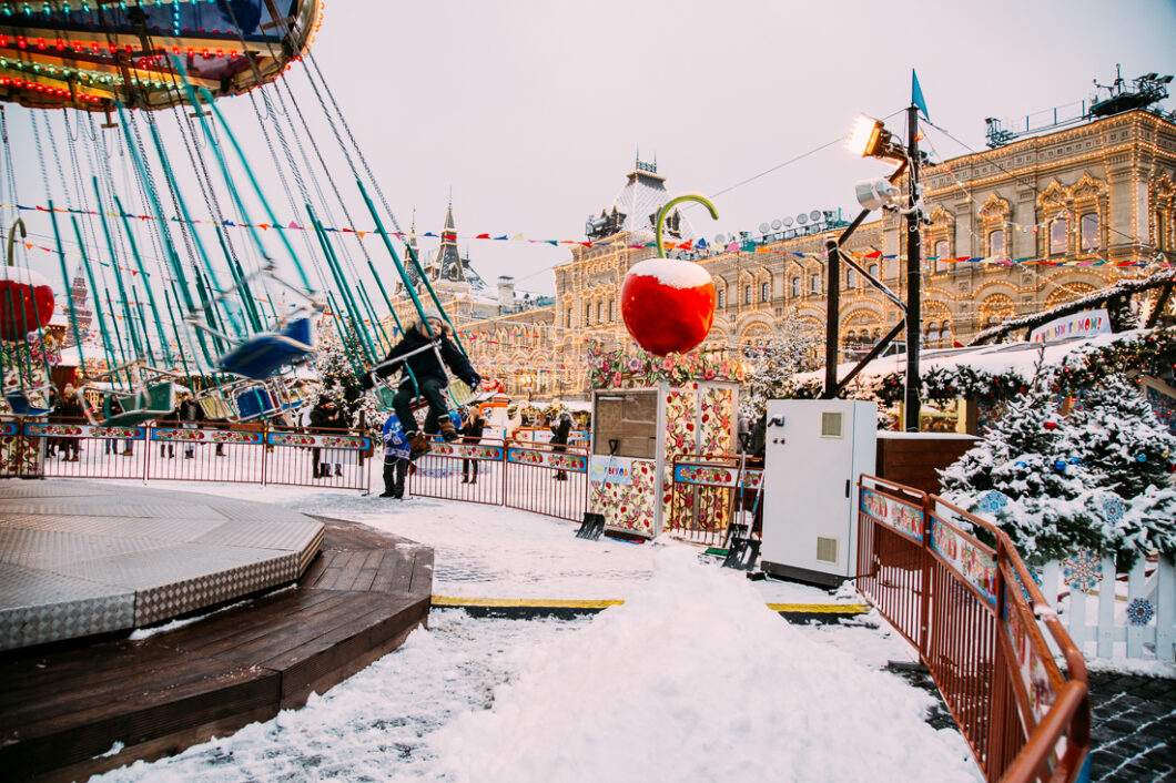 Children ride carnival rides at the Moscow Christmas Market, with the light-adorned Russian Embassy building on the street in the background.