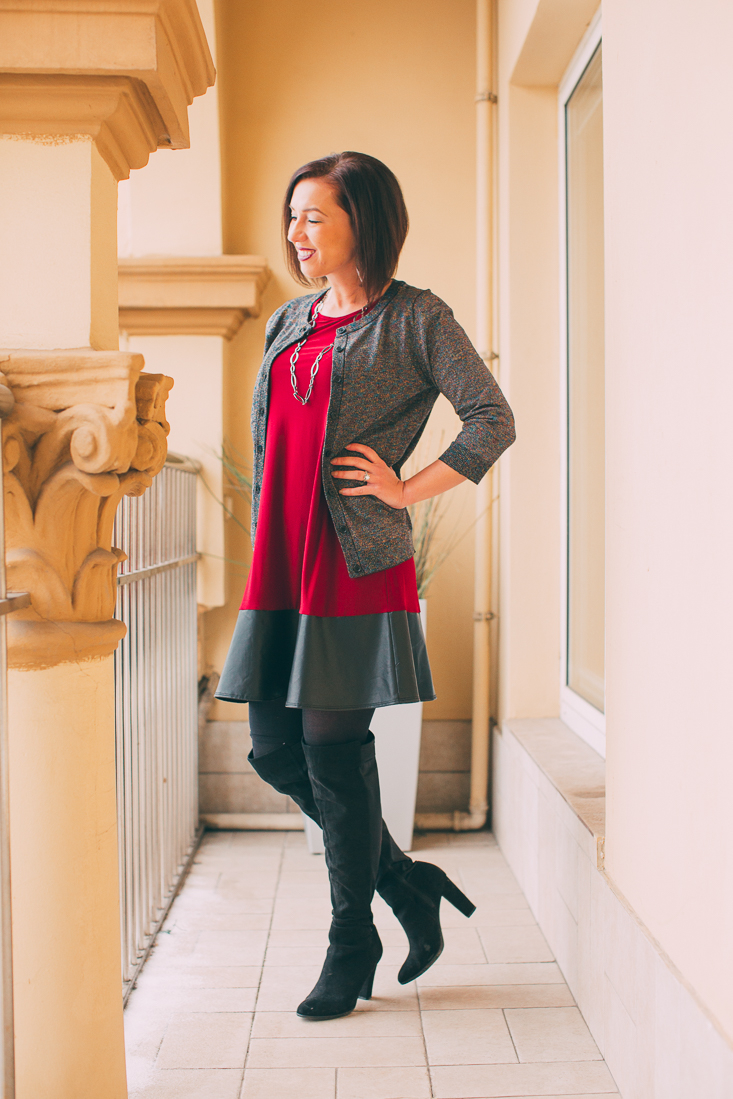 Lindsey wearing a sparkly cardigan with red dress and leather trim paired with black tights black OTK boots standing on an apartment balcony