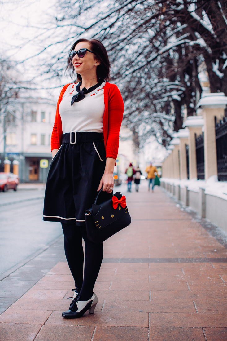A Hello Kitty outfit featuring hello kitty bag, blouse, red cardigan, and black tights