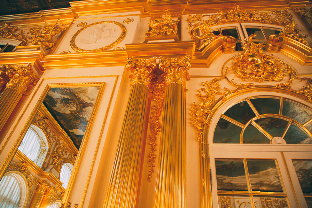 two giant gold columns adorn a wall inside Catherine Palace in Russia, surrounded by gold molding around doorways, mirrors, and lining the ceiling.