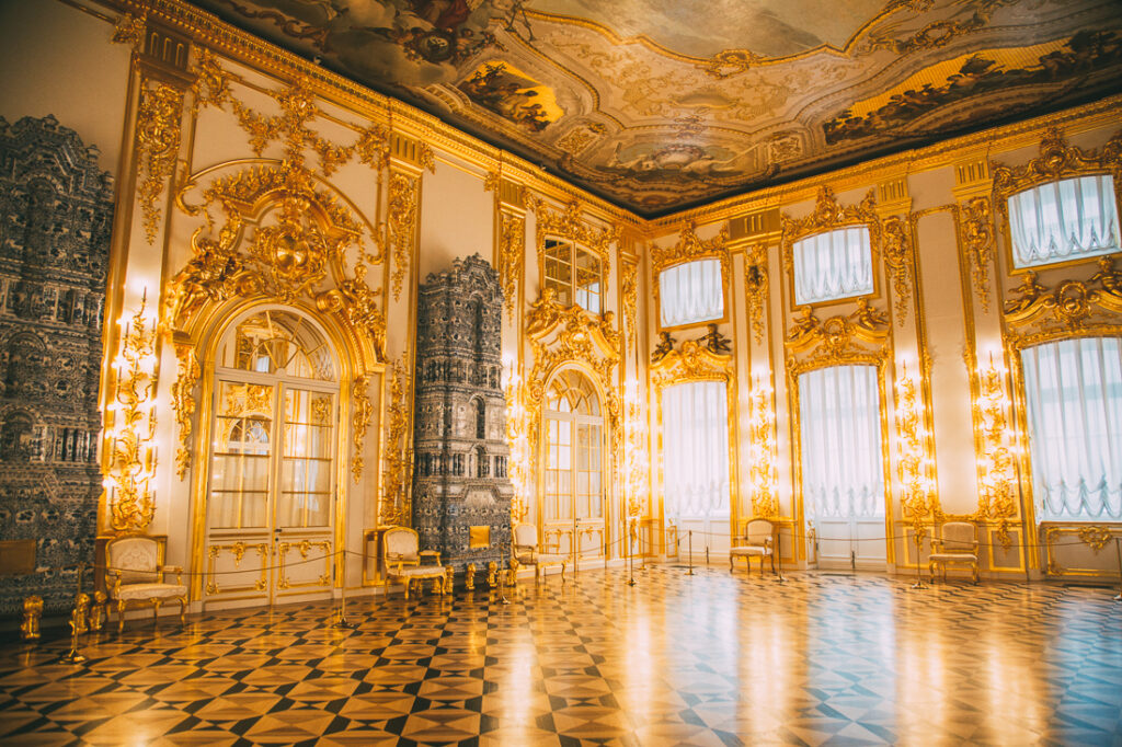 An interior image of an empty ballroom inside Catherine Palace, with high ceilings and walls full of windows, surrounded by gold crown molding.